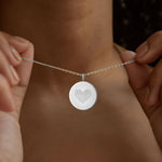 The Danibydsgn Heart Fingerprint Coin Necklace in 925 Sterling Silver being gently held close — featuring two fingerprints forming a heart, symbolising love, connection, and cherished memories in fine minimalist jewelry.