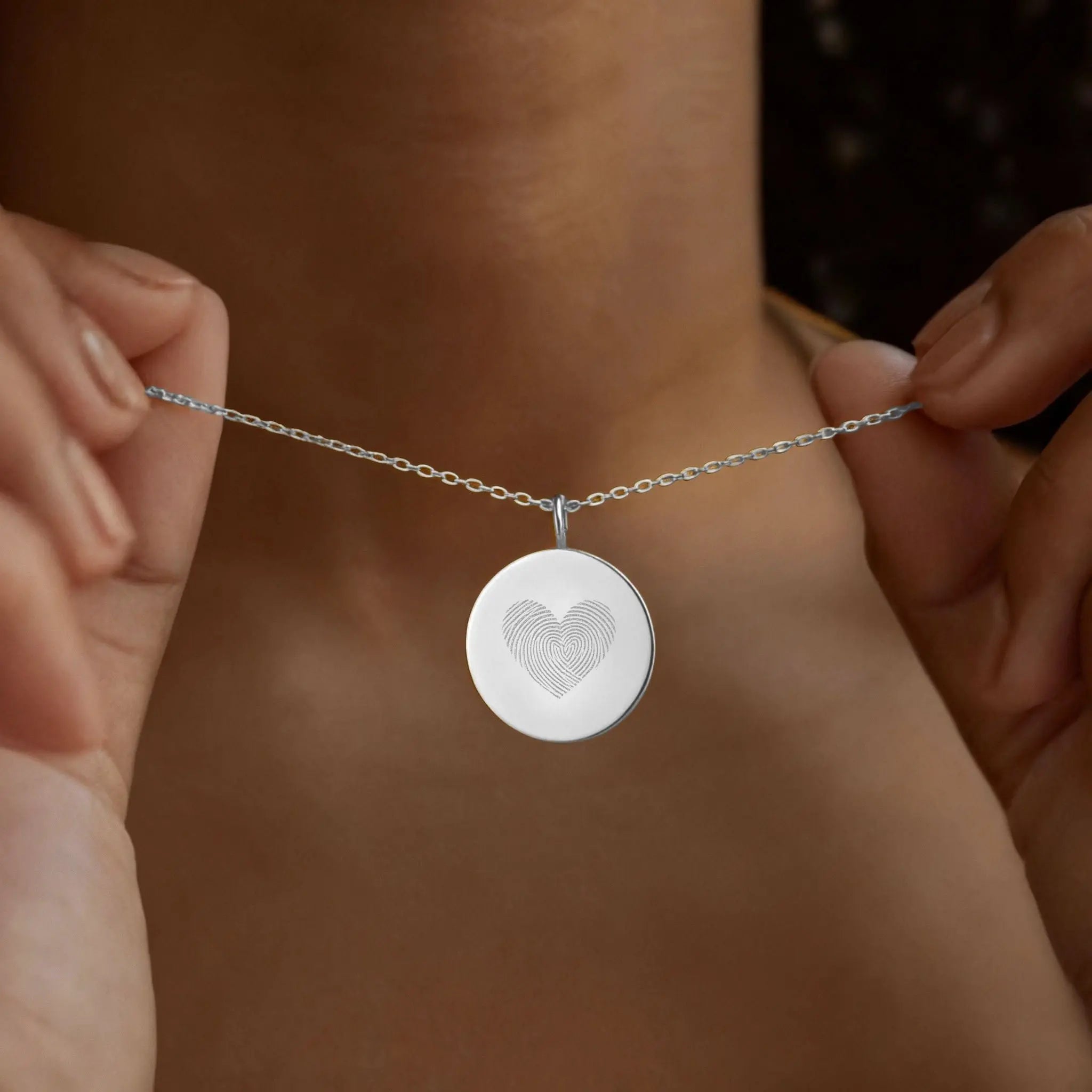 The Danibydsgn Heart Fingerprint Coin Necklace in 925 Sterling Silver being gently held close — featuring two fingerprints forming a heart, symbolising love, connection, and cherished memories in fine minimalist jewelry.