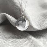 The Danibydsgn Heart Fingerprint Coin Necklace in 925 Sterling Silver resting on soft fabric — featuring two fingerprints engraved into a heart shape, symbolising love, unity, and timeless elegance in fine personalized jewelry.