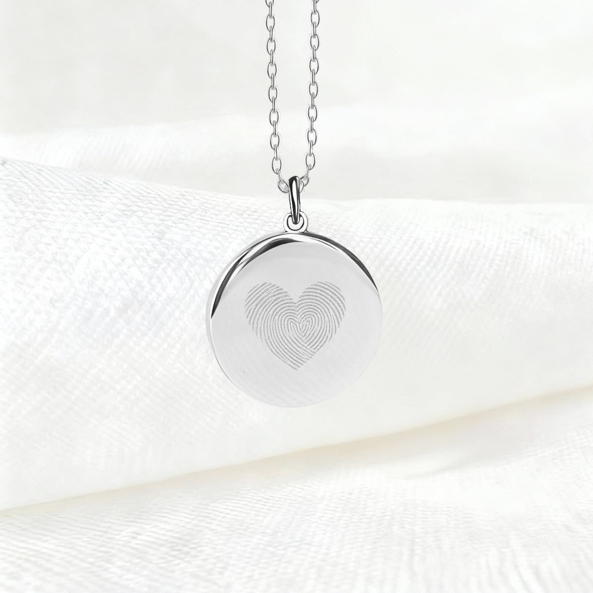 Danibydsgn Heart Fingerprint Pendant Necklace in 925 Sterling Silver displayed on soft white fabric, featuring two fingerprints elegantly engraved to form a heart — a minimalist and meaningful symbol of love and connection.