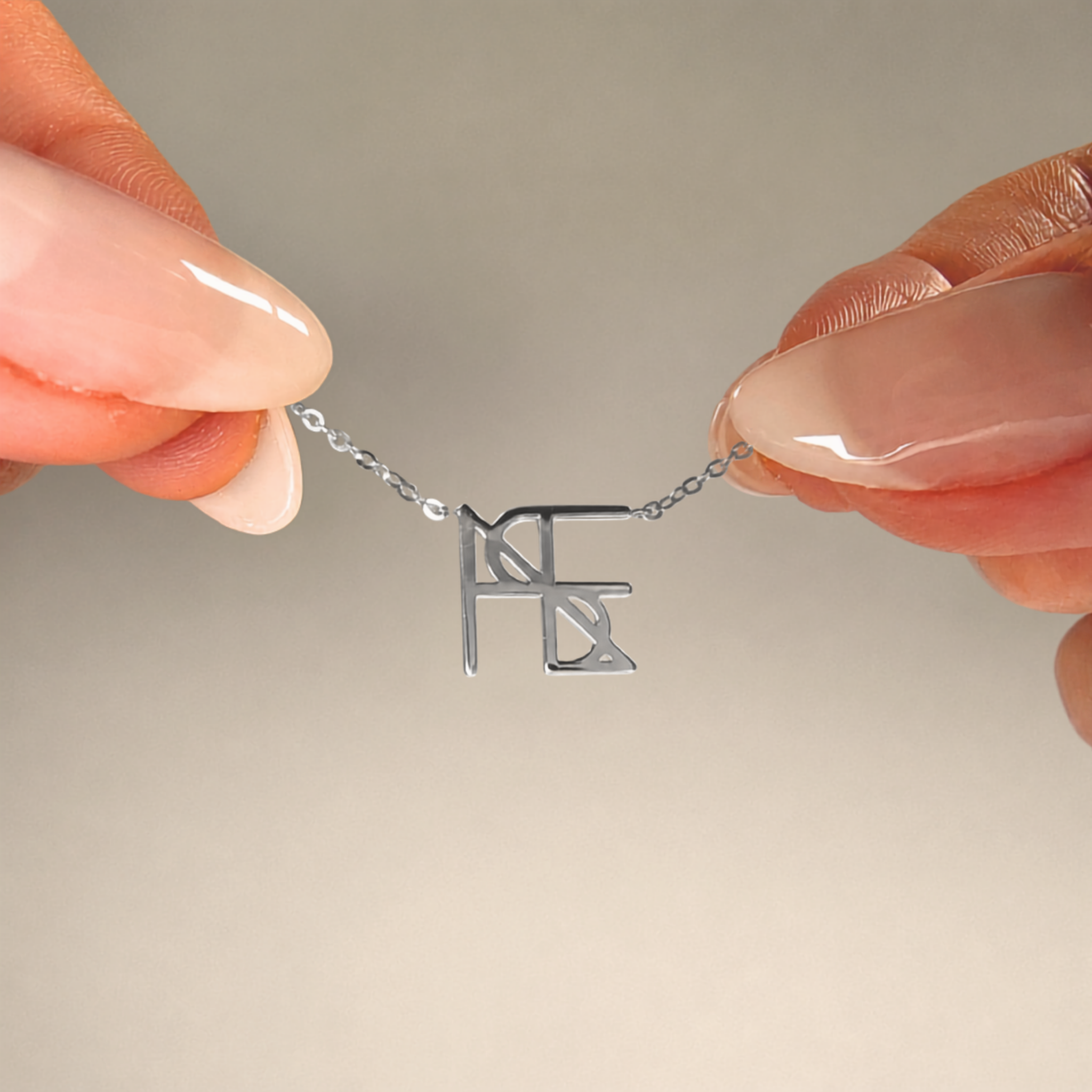 A detailed macro product shot of a model's fingers holding up the sides of a delicate silver chain to display a Danibydsgn single symbol pendant necklace in 925 sterling silver. The close-up showcases a personalized uppercase geometric initial charm handcrafted from a custom line art design against a clean, neutral background.