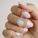 Close-up of the Danibydsgn Single Fingerprint Coin Bracelet in 925 Sterling Silver, featuring a polished circular pendant engraved with a single fingerprint design, held delicately between fingers to highlight its fine chain and engraved detail.