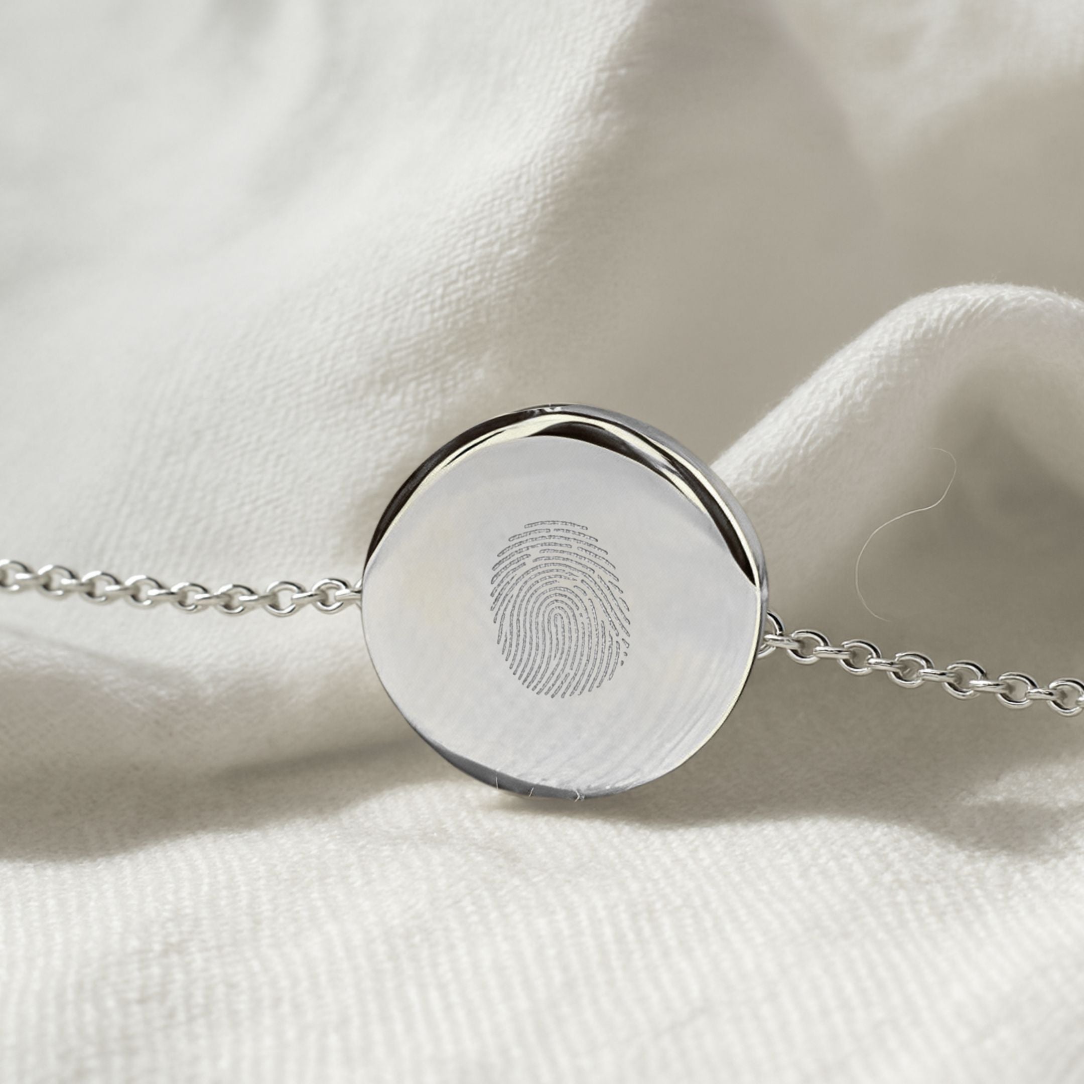 Close-up of Danibydsgn Single Fingerprint Coin Bracelet in 925 Sterling Silver, showing the finely diamond-engraved fingerprint detail on the polished 16mm coin pendant against a soft white fabric background.