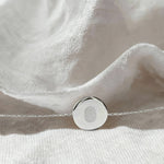 Elegant flatlay of the Danibydsgn Single Fingerprint Coin Bracelet in 925 Sterling Silver resting on white linen fabric, highlighting the engraved fingerprint pendant and delicate chain under soft natural light.