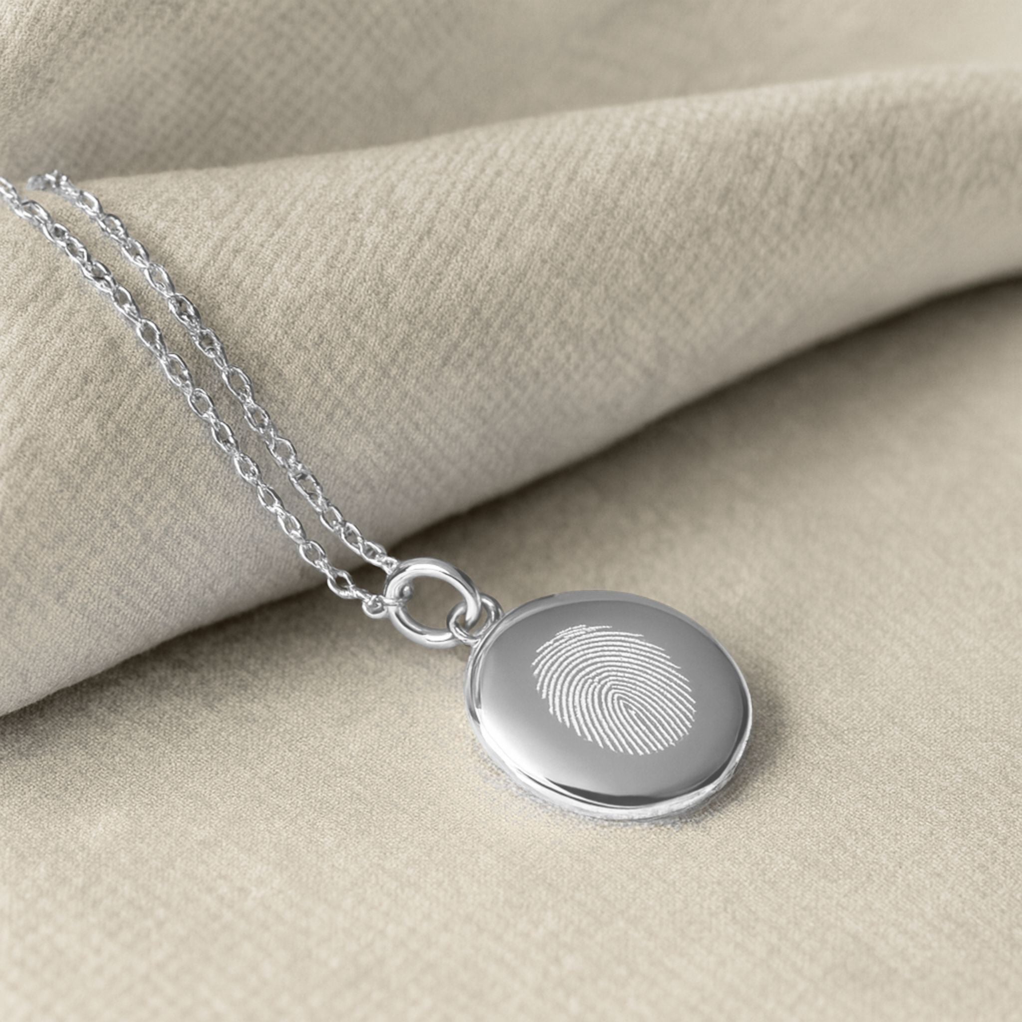 Elegant close-up of the Danibydsgn Single Fingerprint Necklace in 925 Sterling Silver, displayed on soft neutral fabric — featuring a diamond-engraved fingerprint pendant that captures love and individuality in timeless luxury craftsmanship.