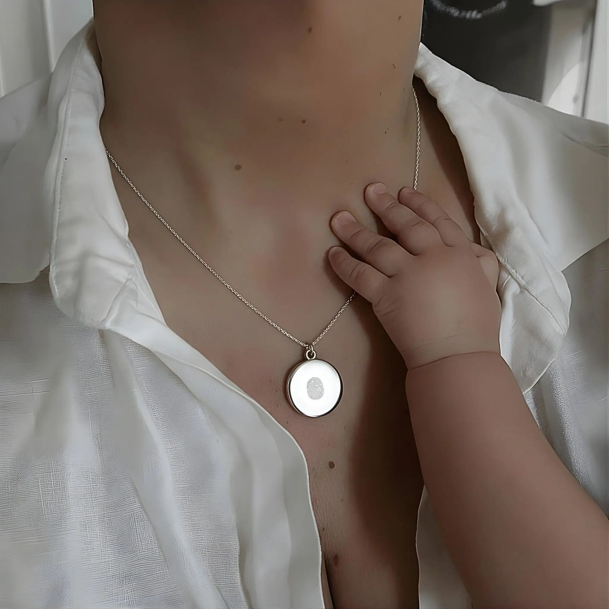 A touching moment showing a mother wearing the Danibydsgn Single Fingerprint Pendant Necklace in 925 Sterling Silver while a baby’s hand gently touches it — a symbol of love, memory, and everlasting connection captured in fine personalized jewelry.