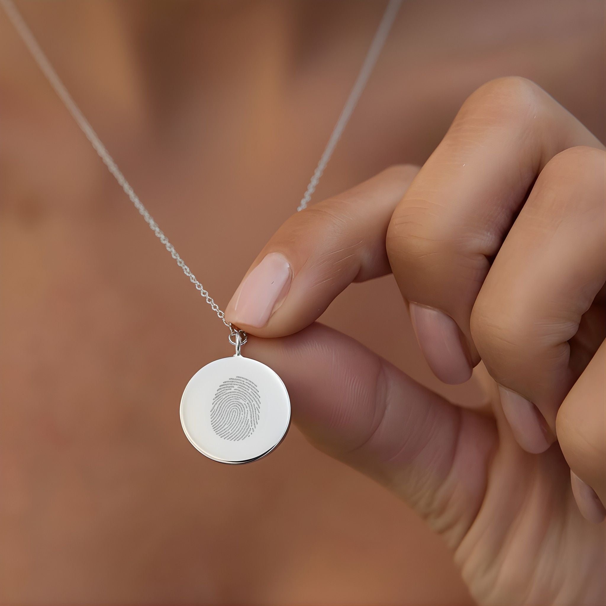 A close-up of the Danibydsgn Single Fingerprint Coin Necklace in 925 Sterling Silver being gently held between fingers. The engraved fingerprint detail catches the light, representing a deeply personal bond and the timeless elegance of custom keepsake jewelry.