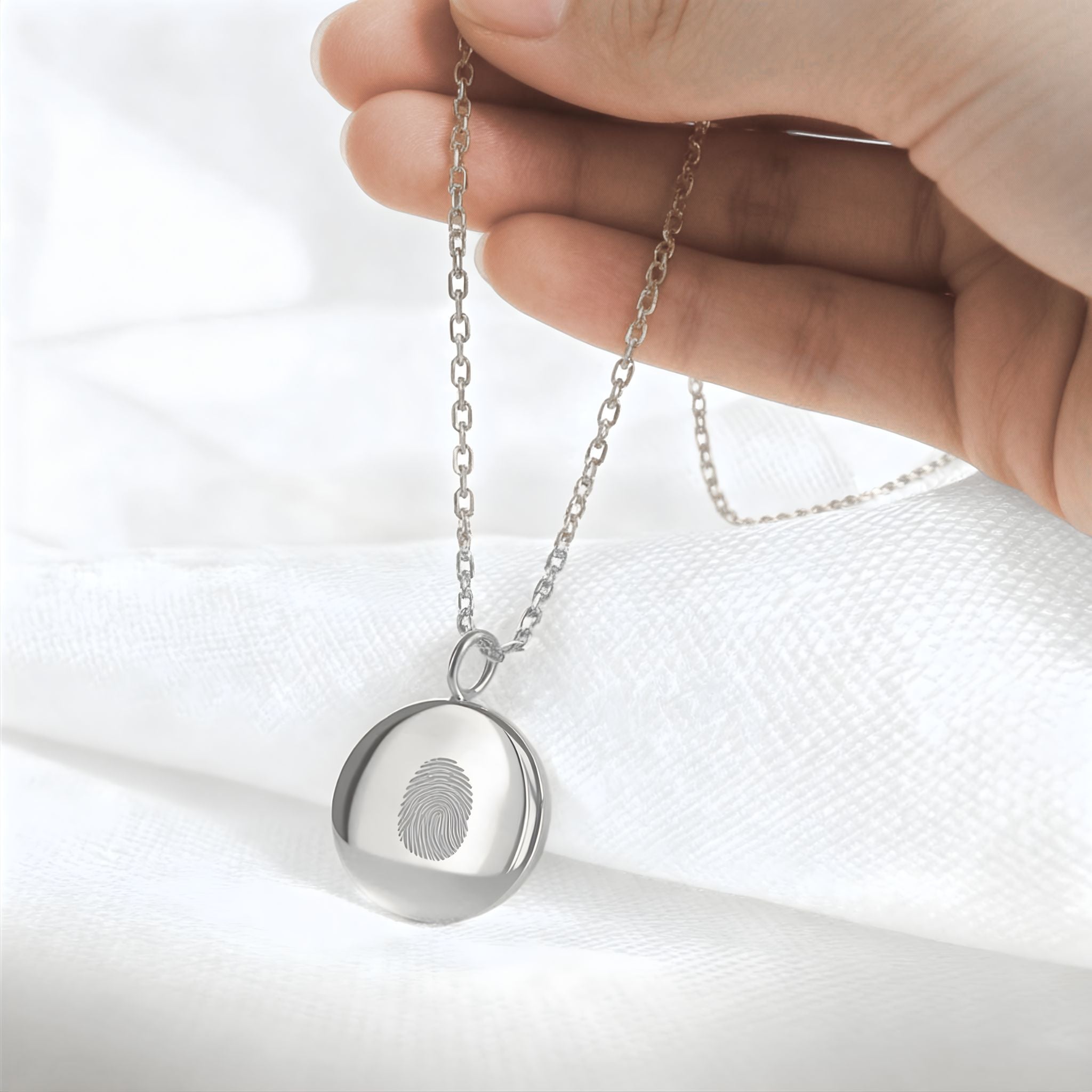 Close-up of the Danibydsgn Single Fingerprint Coin Necklace in 925 Sterling Silver, delicately held by hand against a soft white background. The engraved fingerprint pendant gleams with refined craftsmanship, symbolising cherished memories, identity, and everlasting connection.