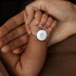 A tender mother-and-child moment featuring the Danibydsgn Single Fingerprint Coin Necklace in 925 Sterling Silver. A baby’s hand holds the elegant fingerprint pendant, symbolising the eternal bond between parent and child. This emotional keepsake captures love, identity, and connection in a timeless silver design.