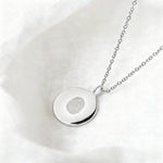 The Danibydsgn Single Fingerprint Coin Necklace in 925 Sterling Silver, resting elegantly on soft white fabric. Its polished surface reflects light beautifully, highlighting the engraved fingerprint — a delicate expression of love, remembrance, and connection.