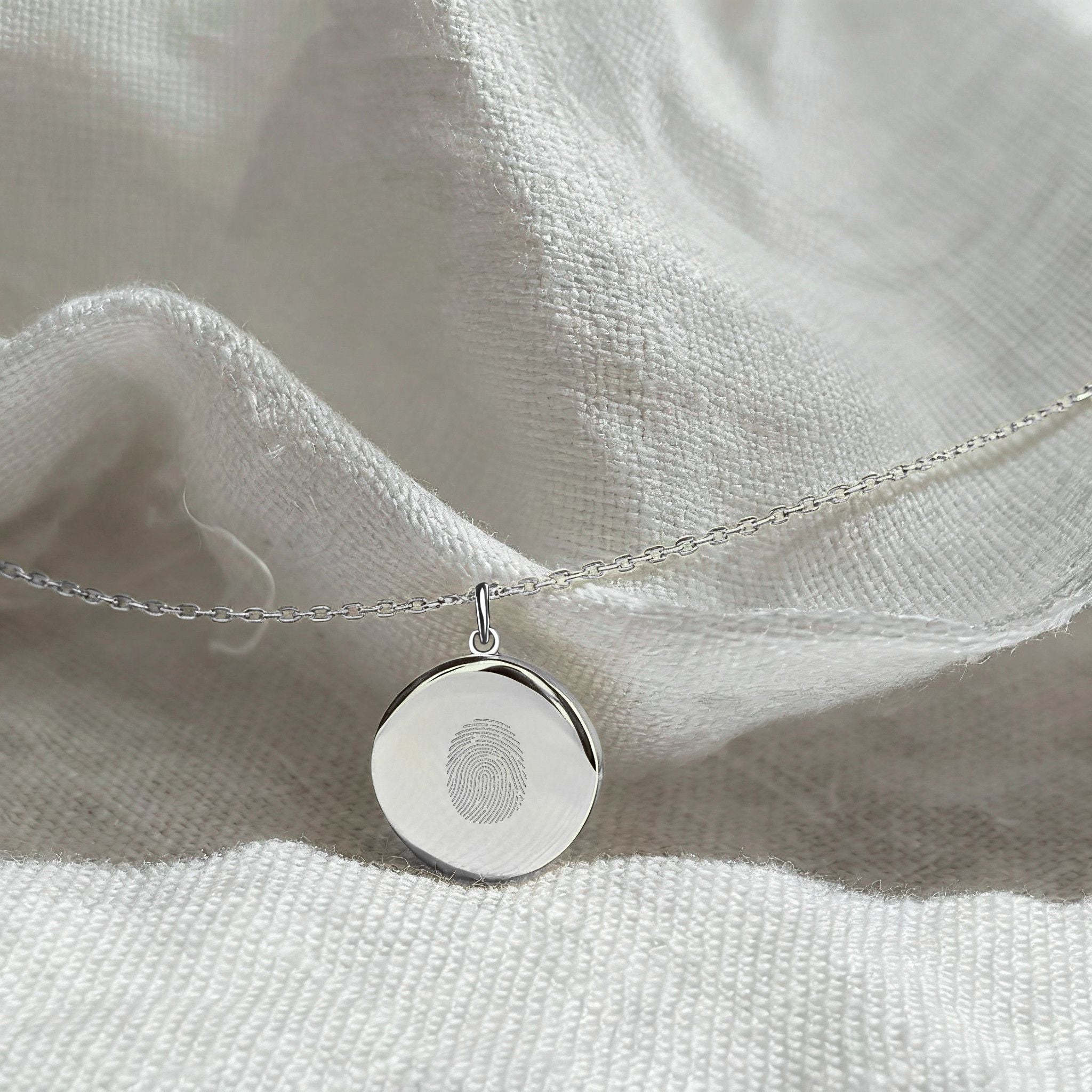 Close-up of the Danibydsgn Single Fingerprint Pendant Necklace in 925 Sterling Silver resting on soft white fabric — showcasing the fine diamond-engraved fingerprint design and elegant minimalist craftsmanship of this personalized keepsake jewelry.