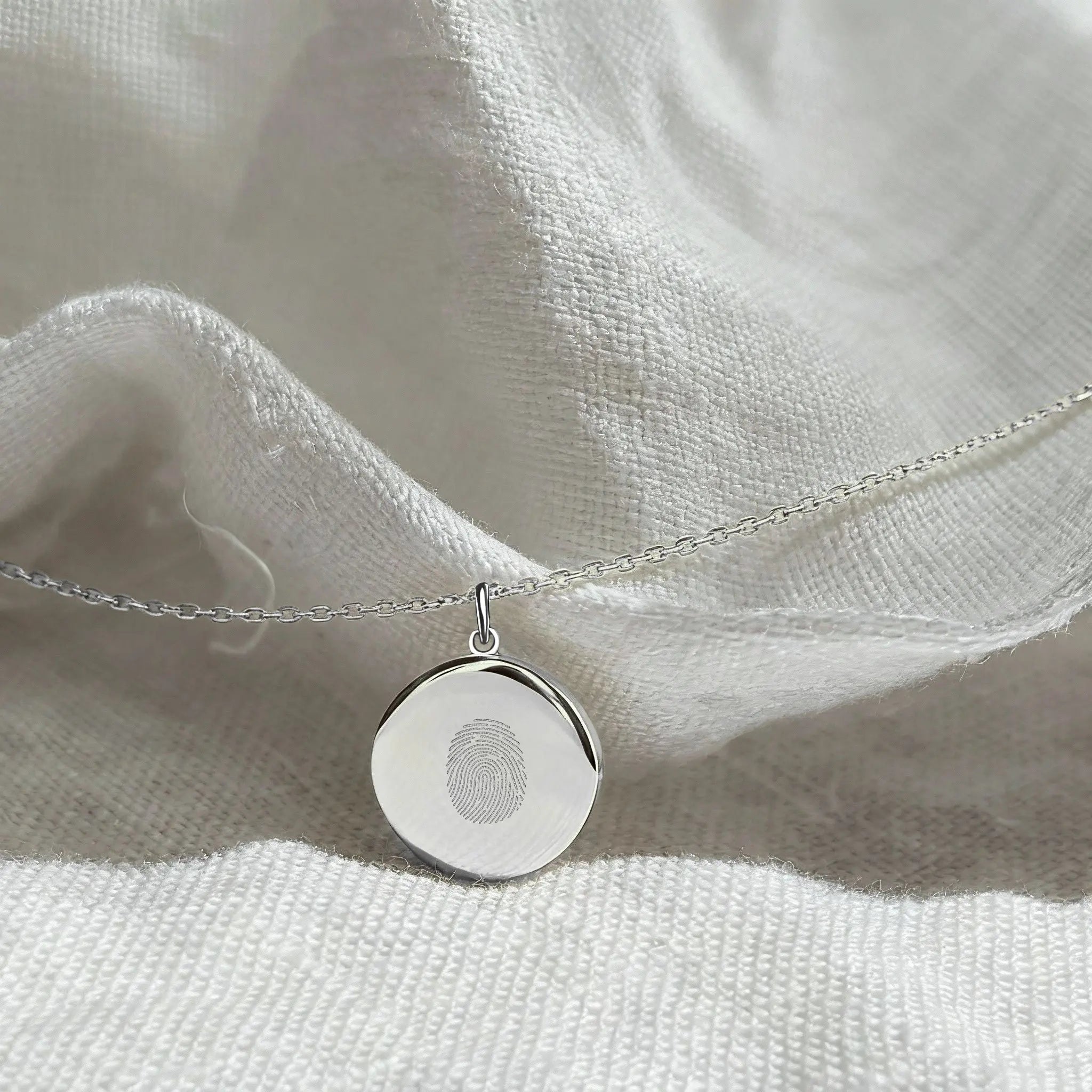 Close-up of the Danibydsgn Single Fingerprint Pendant Necklace in 925 Sterling Silver resting on soft white fabric — showcasing the fine diamond-engraved fingerprint design and elegant minimalist craftsmanship of this personalized keepsake jewelry.