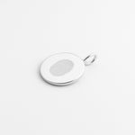 A minimalist flatlay of the Danibydsgn Single Fingerprint Coin Pendant in 925 Sterling Silver. The delicate fingerprint engraving glows softly against the polished silver surface — a refined, personal keepsake capturing a single touch forever.
