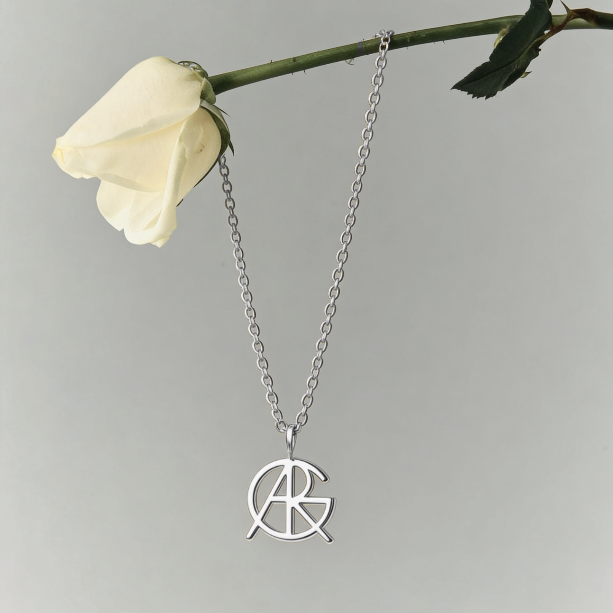 A single symbol jewelry custom necklace made of 925 sterling silver hanging from a white rose, showcasing a piece of meaningful jewelry with a minimalist jewelry cut out jewelry pendant design.