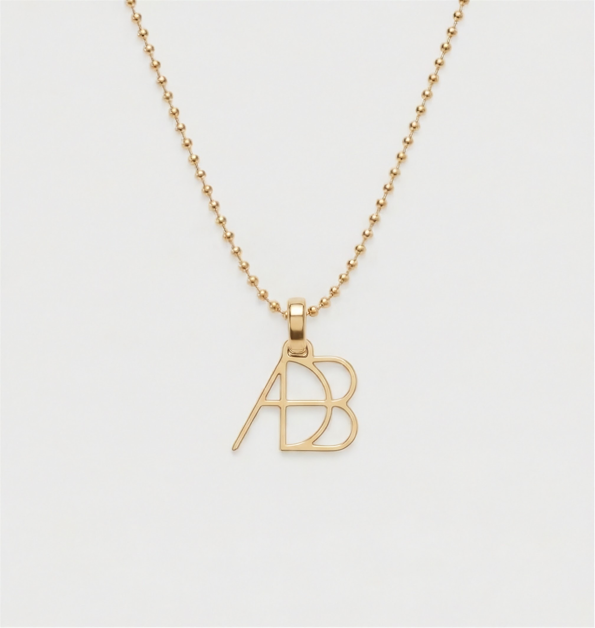 A close up shot of a 9k yellow gold ball chain necklace  and custom Danibydsgn symbol design clip-on charm photographed on a light back ground. Meaningful personalised jewelry from Danibydsgn.