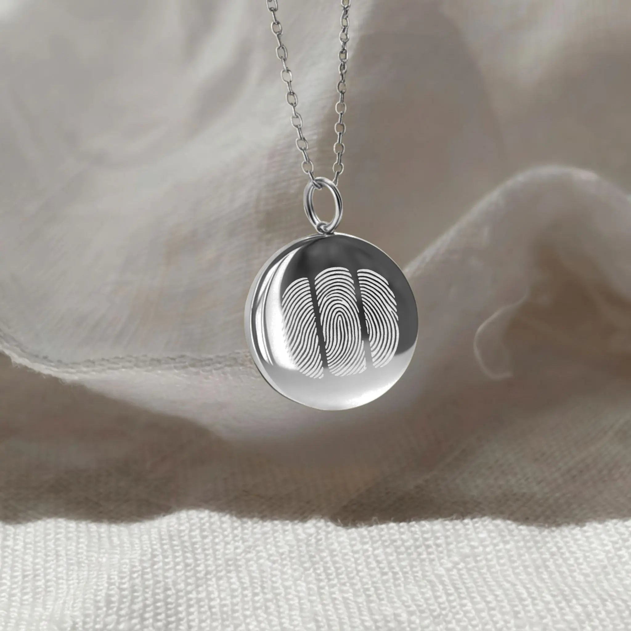 The Danibydsgn Three Fingerprint Coin Necklace in 925 Sterling Silver resting gently against soft fabric, illuminated by natural light — symbolising family, love, and unity through three beautifully engraved fingerprints.