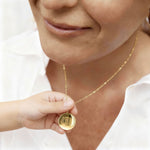 Emotional close-up of a mother and child holding the Danibydsgn Three Fingerprint Coin Necklace in 18K Gold Vermeil. The pendant features three engraved fingerprints symbolising family, love, and connection — a timeless keepsake capturing the bond between mother and child in luxurious, personalised detail.