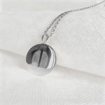 The Danibydsgn Two Fingerprint Coin Necklace in 925 Sterling Silver resting on soft white fabric, showcasing the fine diamond-engraved details of two unique fingerprints — a modern keepsake symbolising love, connection, and timeless craftsmanship.