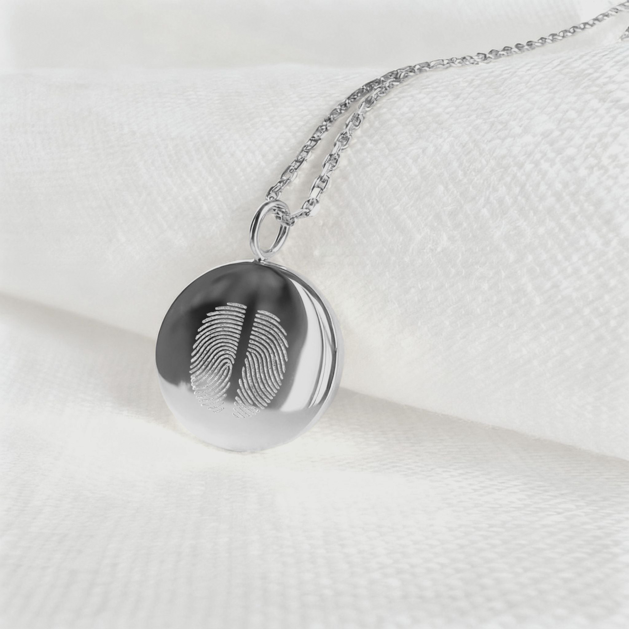 The Danibydsgn Two Fingerprint Coin Necklace in 925 Sterling Silver resting on soft white fabric, showcasing the fine diamond-engraved details of two unique fingerprints — a modern keepsake symbolising love, connection, and timeless craftsmanship.