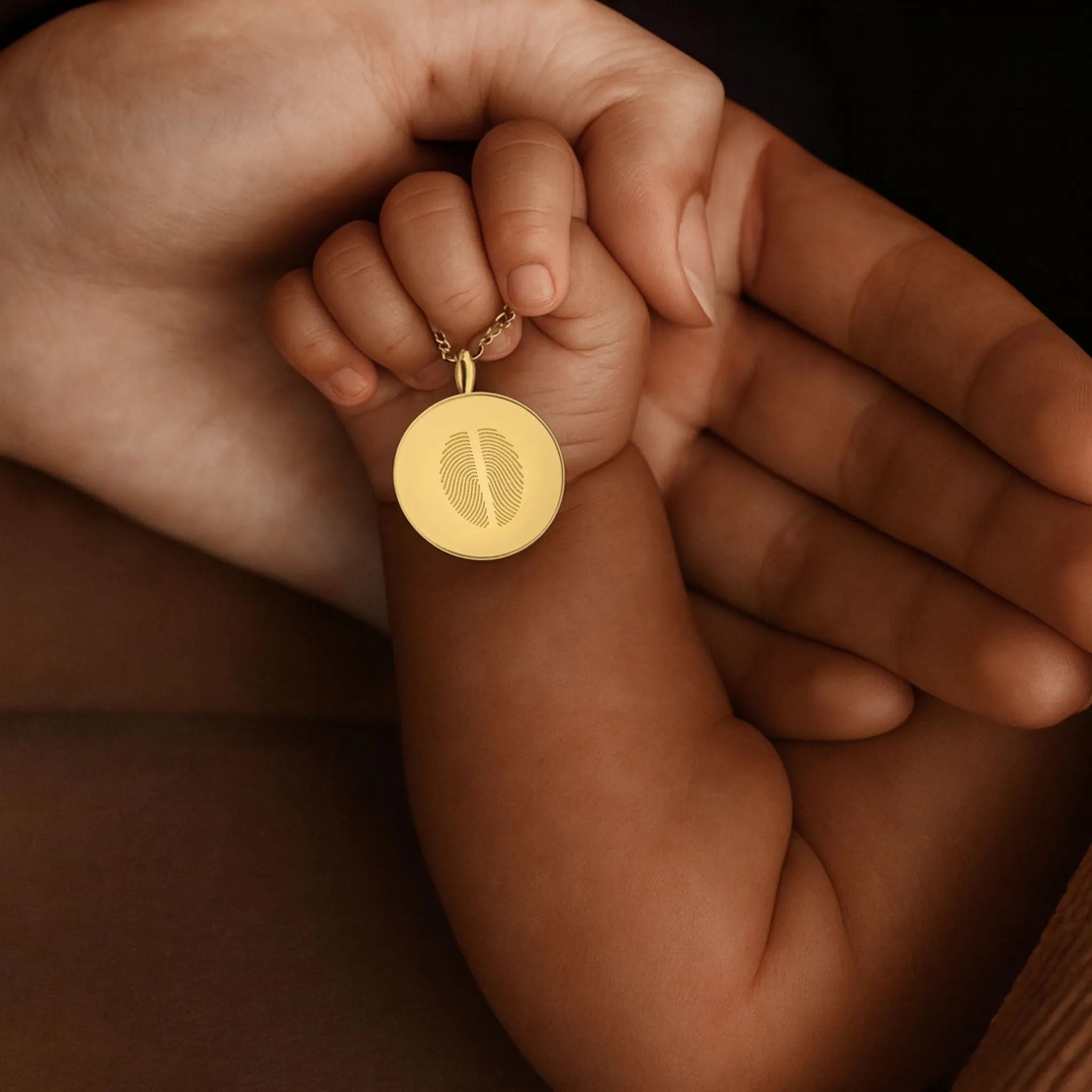 A tender close-up of a baby’s hand resting in their mother’s palm, both holding the Danibydsgn Two Fingerprint Coin Necklace in 18K Gold Vermeil. The pendant features two fingerprints elegantly engraved together, symbolising the unbreakable bond between mother and child — a timeless piece of love, memory, and connection.
