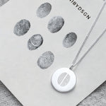 The Danibydsgn Two Fingerprint Coin Necklace in 925 Sterling Silver placed beside real fingerprint imprints — a beautiful reflection of how each piece is thoughtfully engraved to preserve the unique bond and touch between two loved ones.