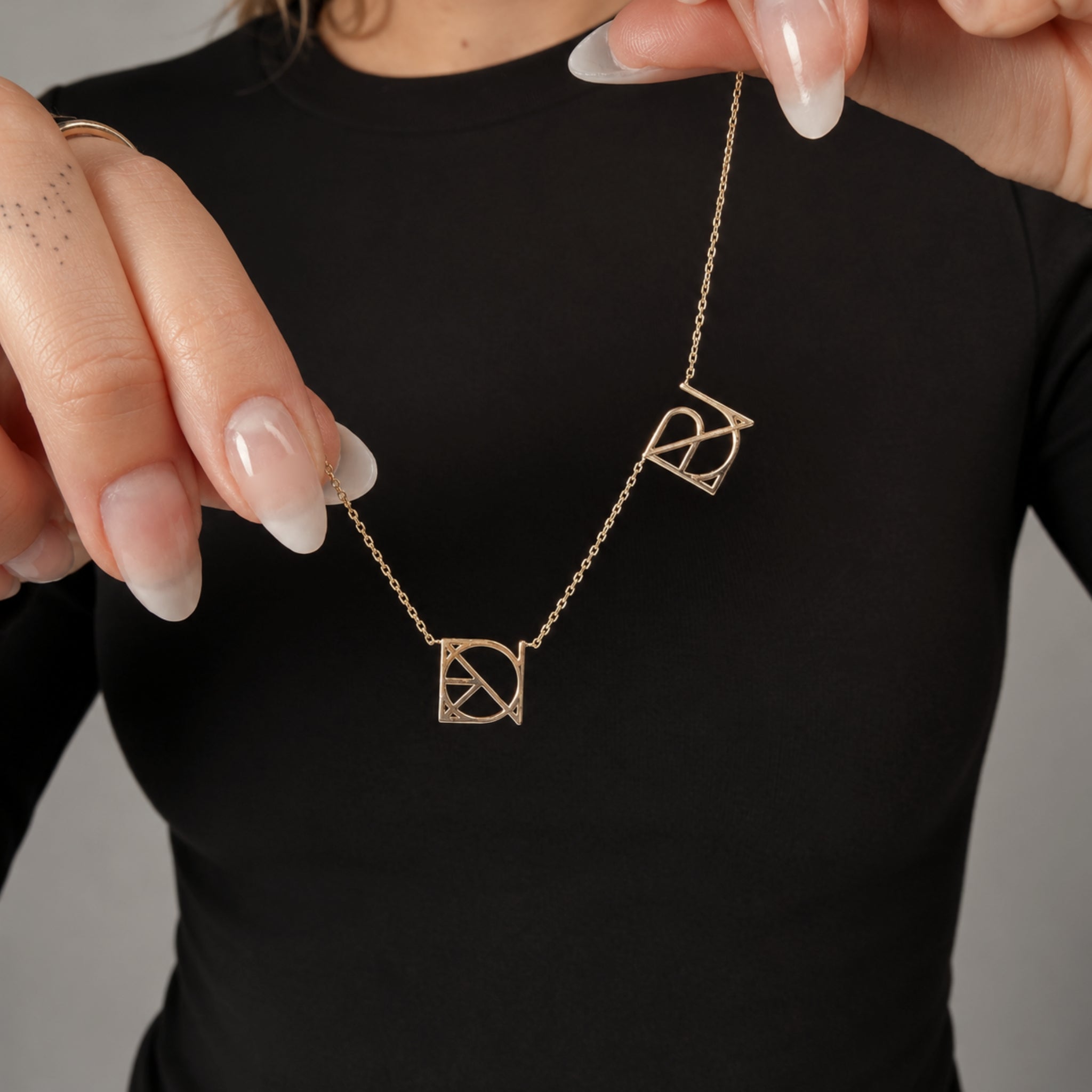 A person holding up a solid 9k gold Danibydsgn custom necklace to showcase two hand-designed symbol jewelry monograms crafted from personal names, dates, or memories to create a piece of meaningful jewelry.