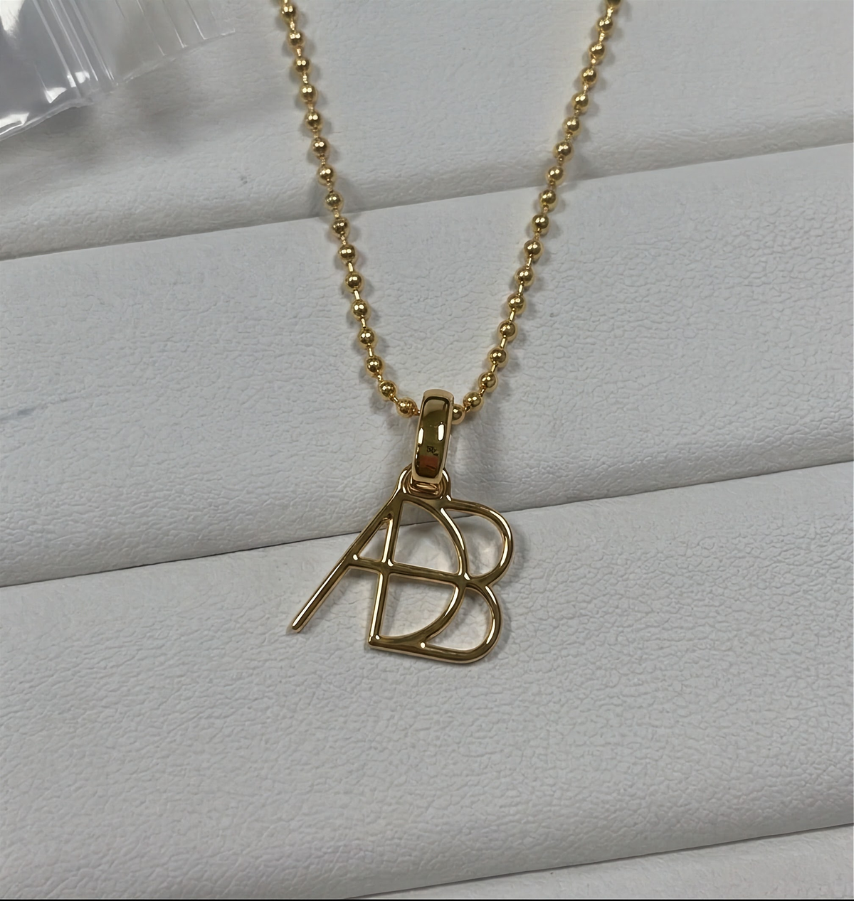 A 9k gold ball chain necklace  and custom Danibydsgn design clip-on charm photographed on a light grey textured surface.  Meaningful personalised jewelry from Danibydsgn.
