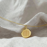 The Three Fingerprint Coin Necklace in 18K Gold Vermeil by Danibydsgn displayed on soft white fabric. The pendant showcases three diamond-engraved fingerprints on a polished gold surface, representing connection, love, and family in a luxurious, minimalist jewelry design.