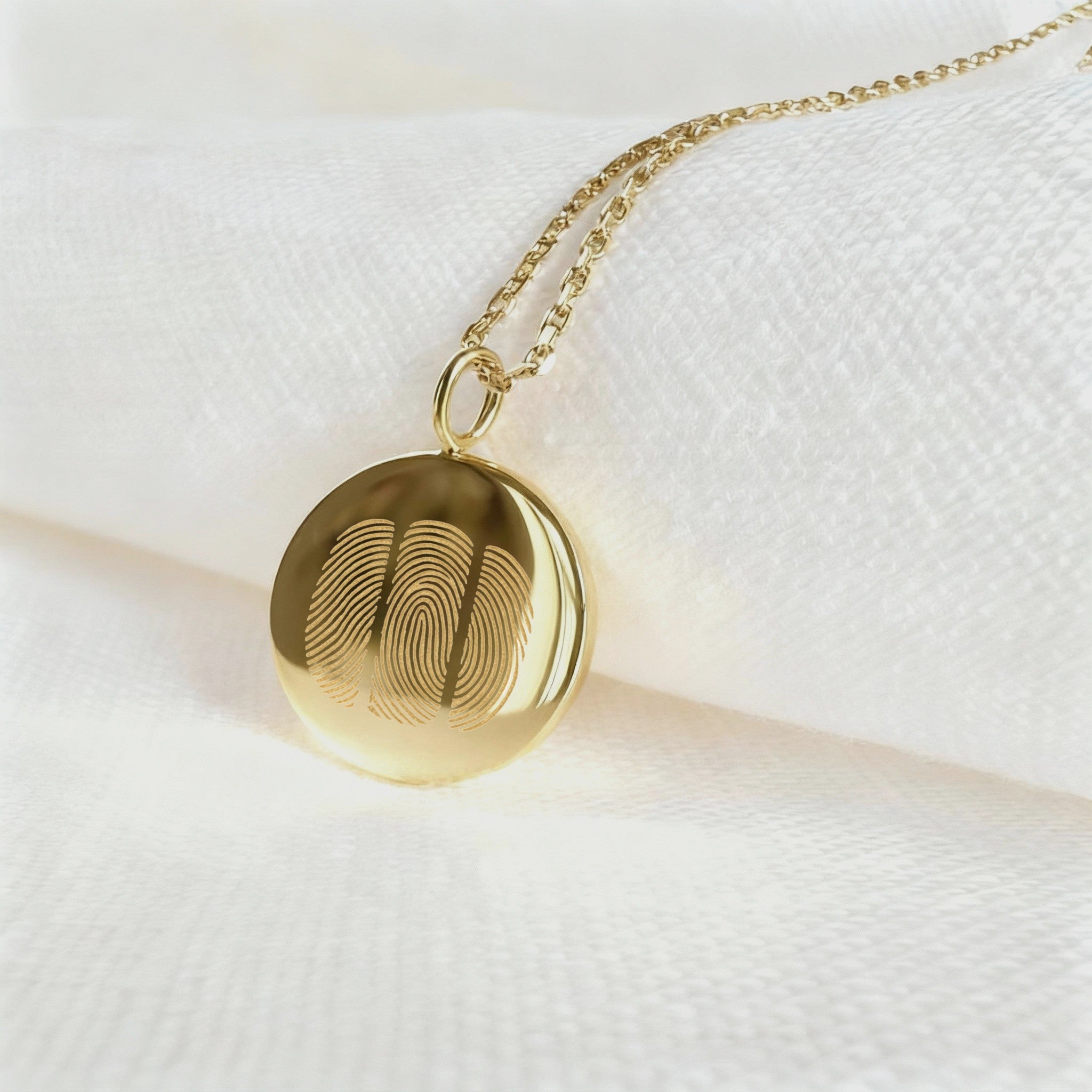 The Luxury Three Fingerprint Coin Necklace in 18K Gold Vermeil by Danibydsgn rests elegantly on a white fabric background. Featuring three detailed fingerprints engraved into a polished gold pendant, this handcrafted piece symbolizes love, memory, and connection in timeless luxury jewelry design.