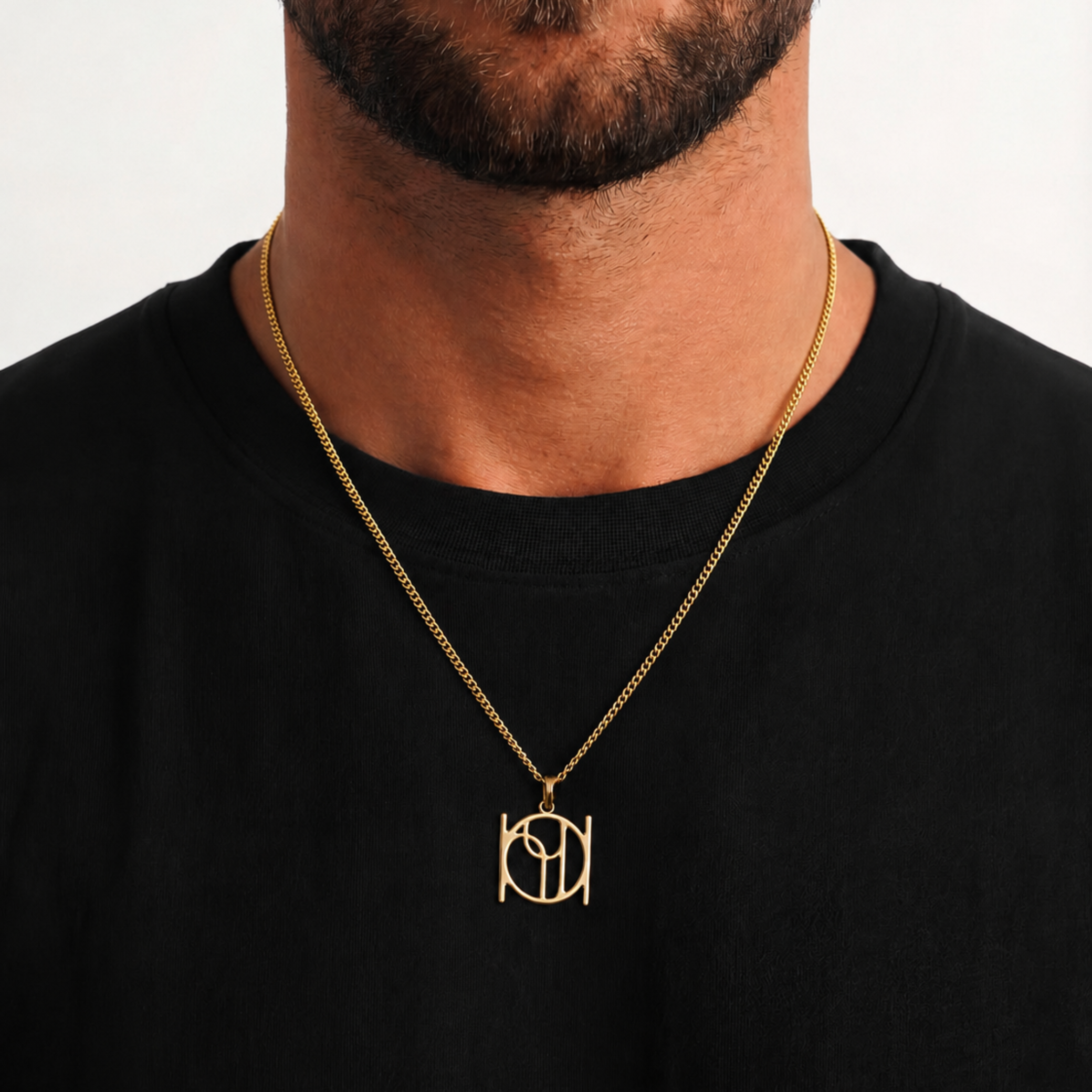 A 9k cable chain necklace with a Danibydsgn custom symbol pendant necklace in 9k yellow gold, worn by a man in a black t-shirt.  Longer chain that rests chest level.
