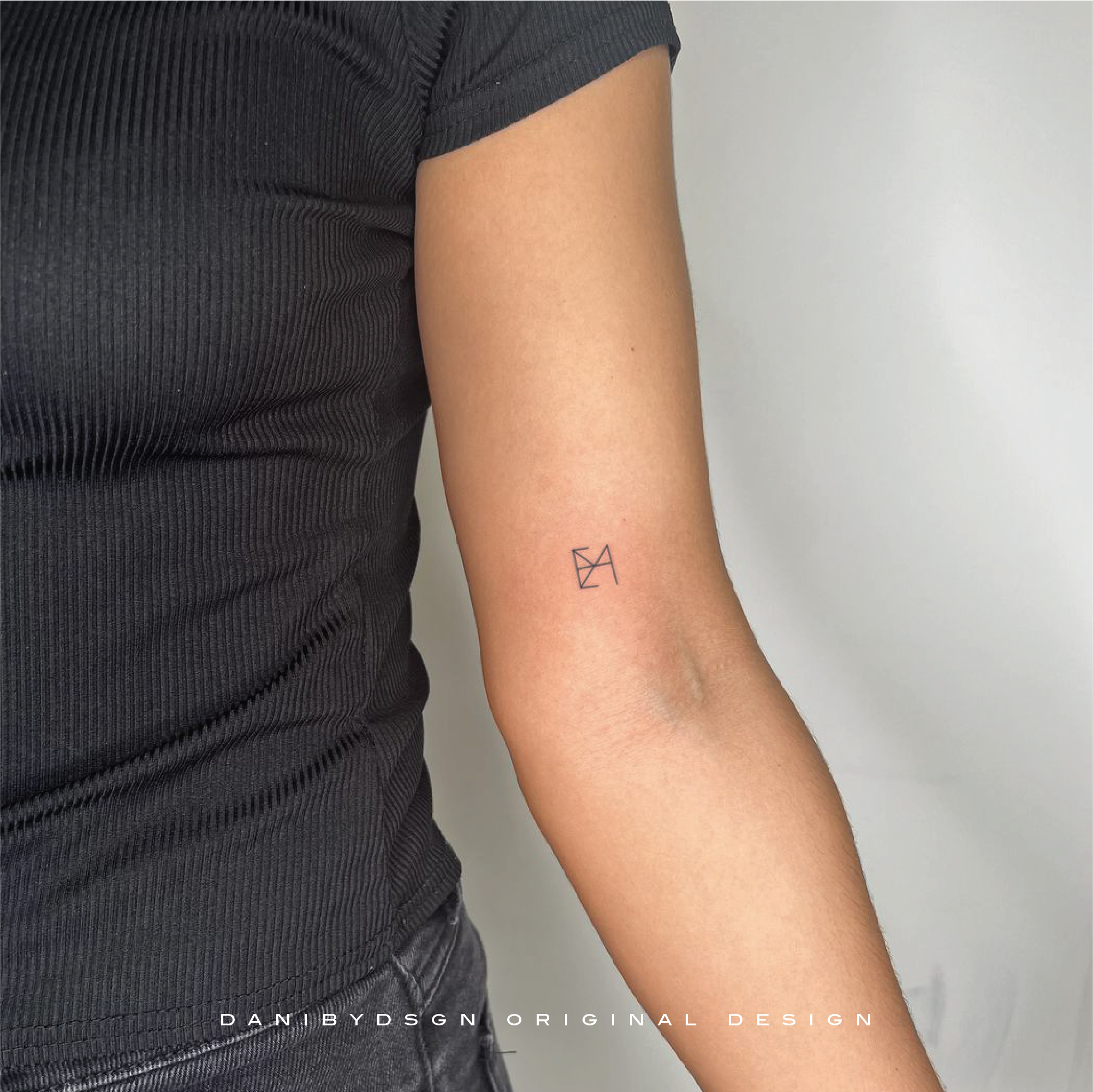 A delicate fine line tattoo design featuring a customized monogram with interlocking letters and intricate details